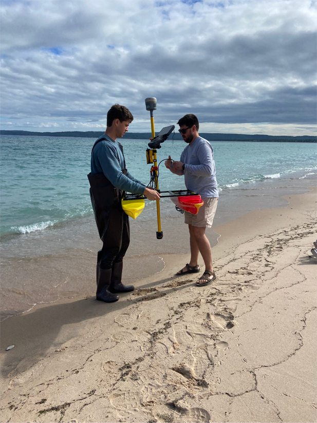 Two people handling a scientific sensor on the beach