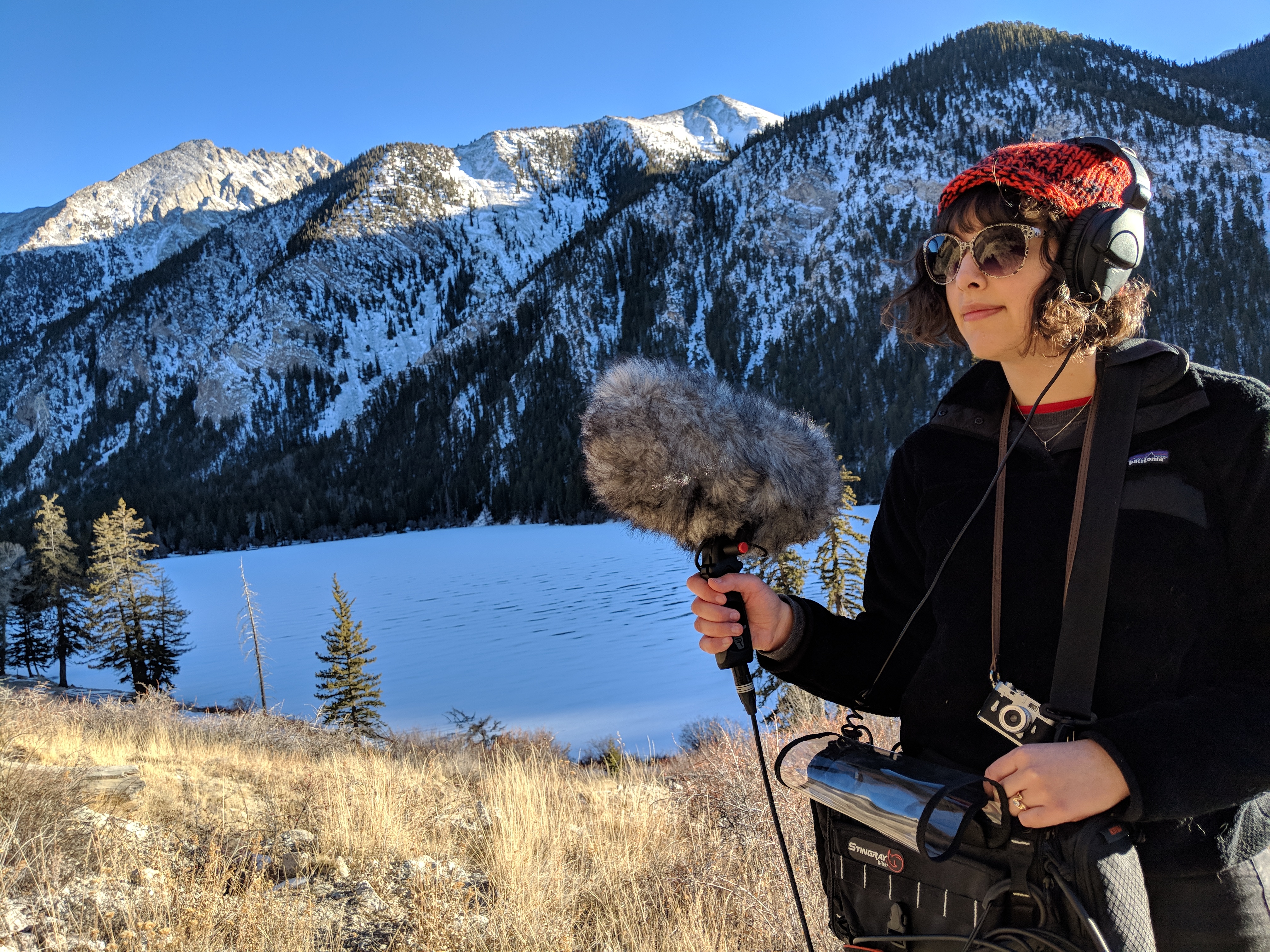 Marinna stands above a frozen lake holding sound recording equipment.