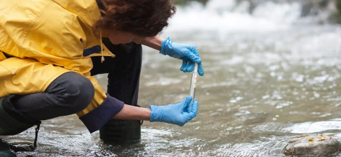 A researcher in a yellow coat testing for PFAS in water