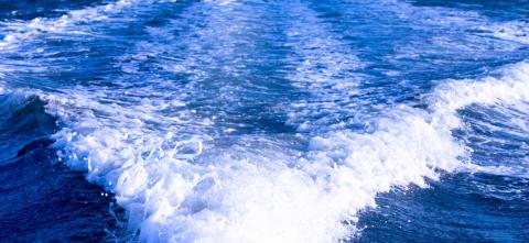 Blue lake water with foamy white waves trailing behind a moving boat.