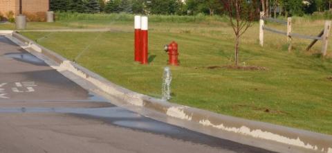 Water flows from a pipe into a curbside drainage area near a fire hydrant.